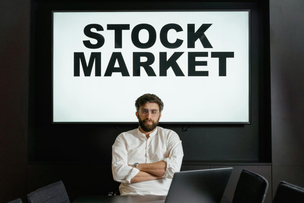 A man sitting confidently in front of a large screen displaying the words Stock Market during a business meeting.