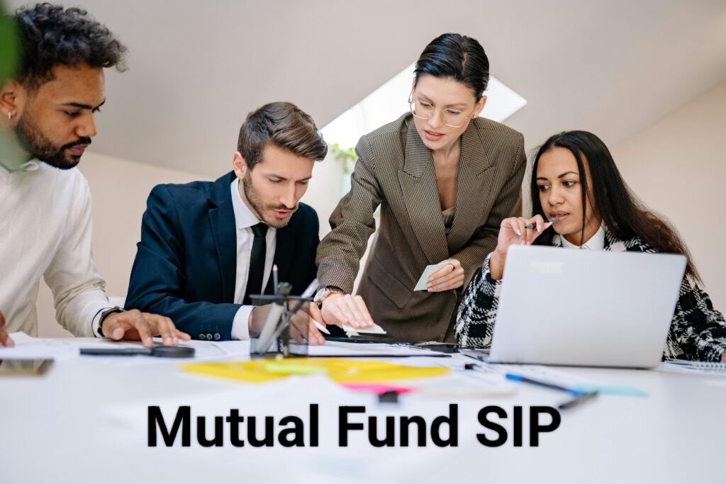 A group of four diverse professionals in business attire collaborating around a table with documents, a laptop, and sticky notes, discussing Mutual Fund SIP investments in a modern office setting.